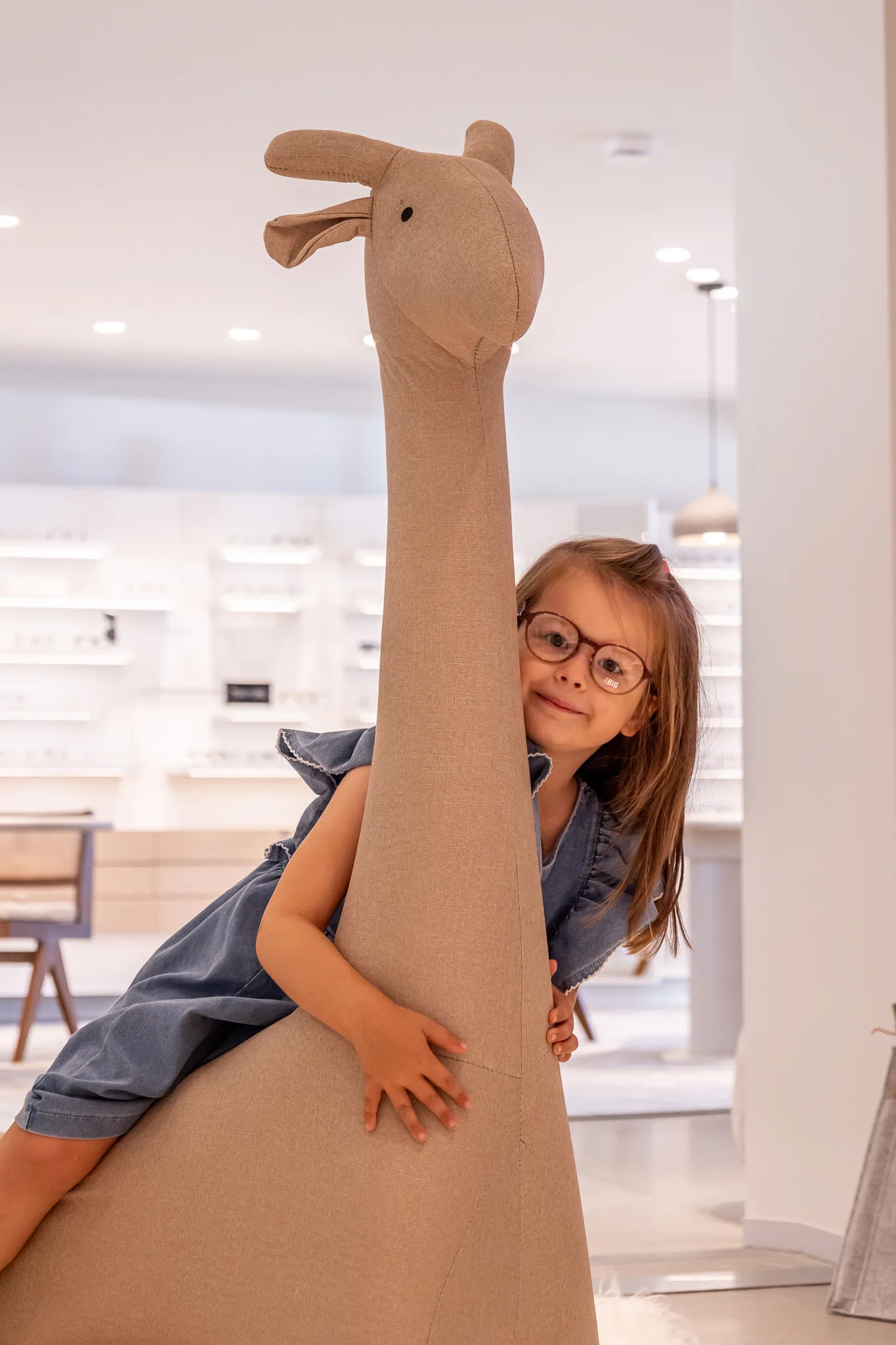 Meisje met een kinderbril piept lachend achter de giraf vandaan